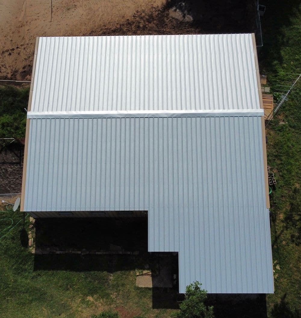 Aerial view of a metal roof on a house with green surroundings and dirt area.