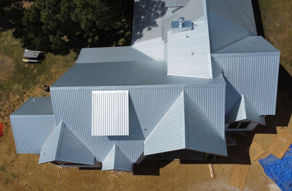 Aerial view of a modern home with a multi-pitched metal roof and outdoor work area.