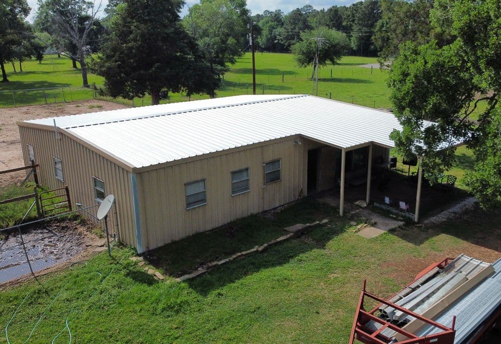 Aerial view of a metal-roofed house surrounded by lush greenery and open fields.