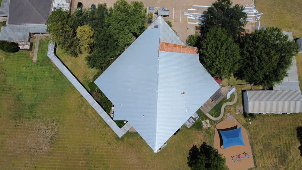 Aerial view of a large building with a pyramid roof, adjacent playground, and green landscape.