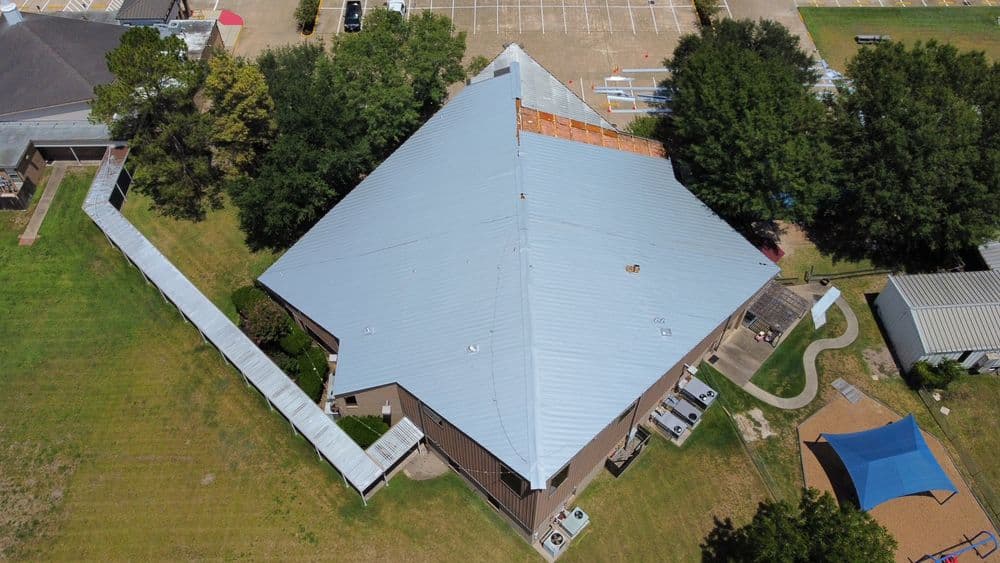 Aerial view of a large building with a metal roof surrounded by green grass and trees.