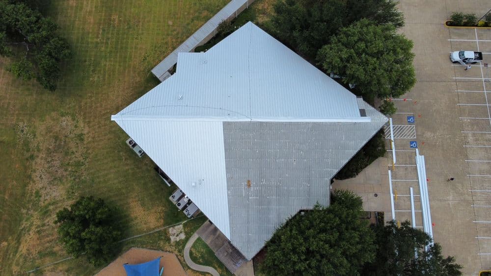 Aerial view of a modern building with a metal roof and surrounding green landscape.