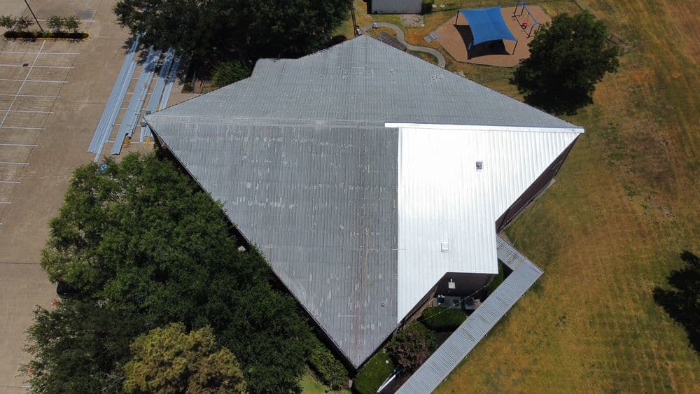 Aerial view of a large building with a metal roof and surrounding green space.