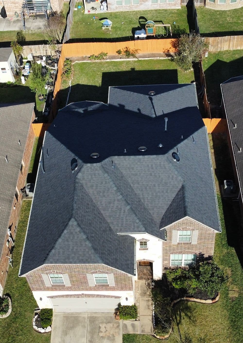 Aerial view of a residential home with a dark shingle roof and well-maintained yard.