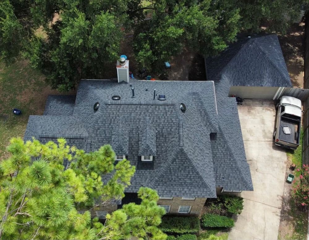 Aerial view of a modern home with a grey shingle roof surrounded by greenery.