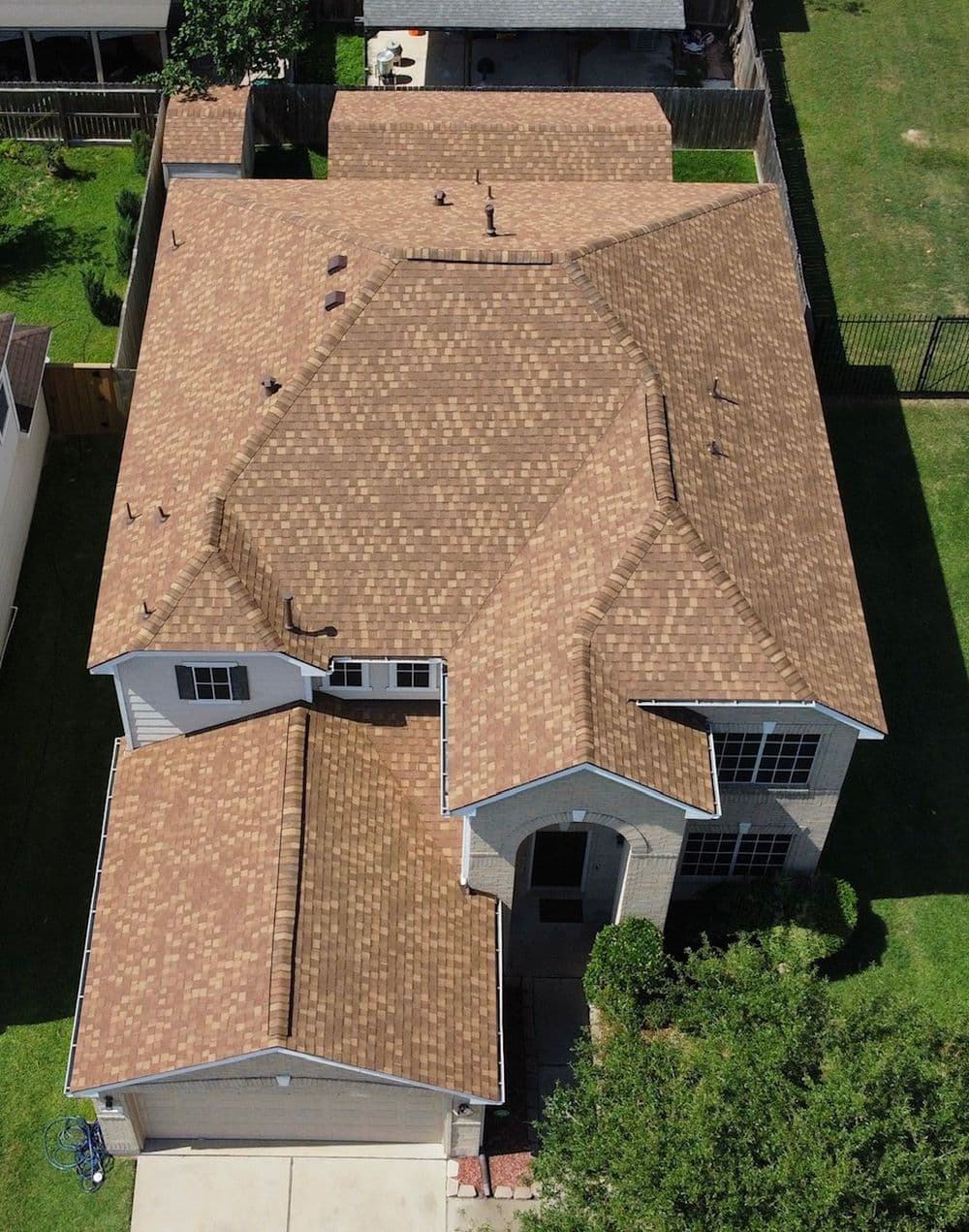Aerial view of a suburban house with a brown shingle roof and landscaped yard.