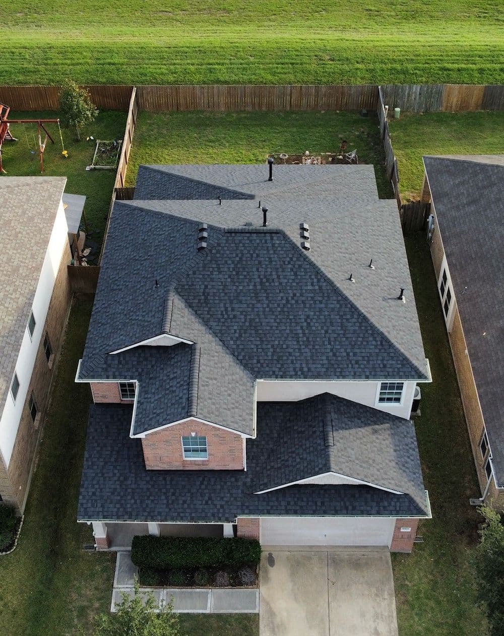 Aerial view of a home with a dark shingle roof and landscaped yard, showcasing residential architecture.