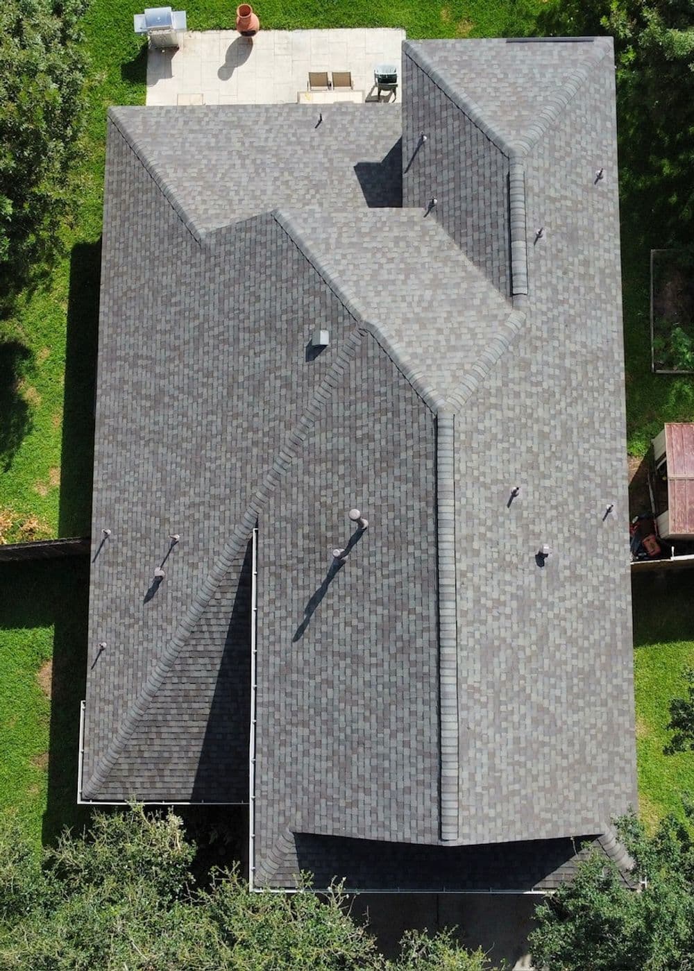 Aerial view of a gray shingle roof on a house surrounded by greenery.