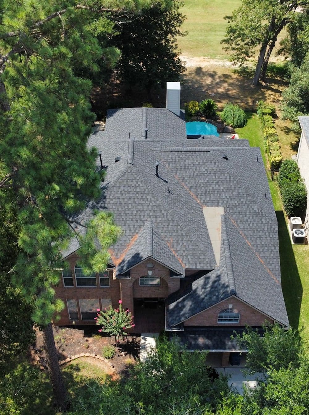 Aerial view of a spacious brick home with a dark shingle roof and lush surrounding landscape.