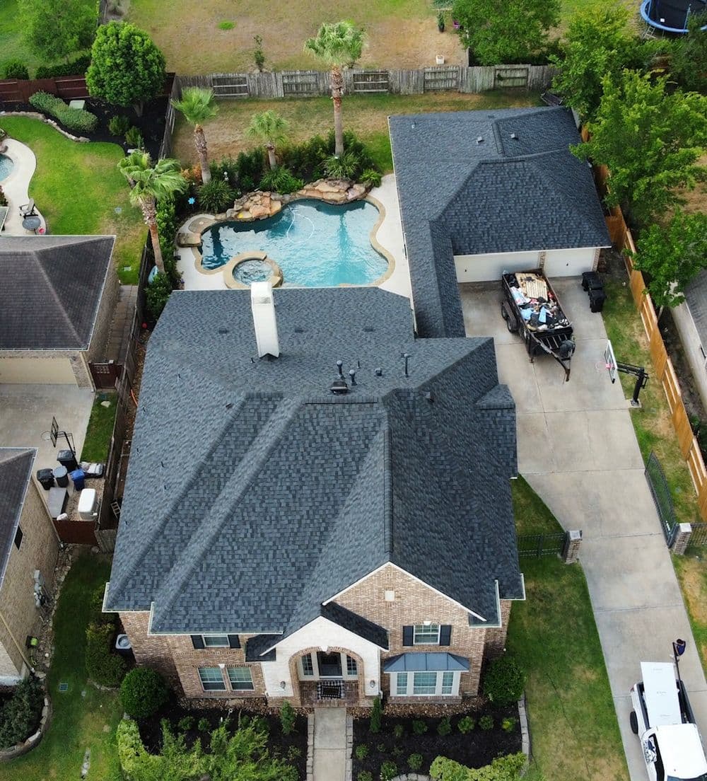 Aerial view of a suburban home with a pool, palm trees, and a garage in a landscaped yard.