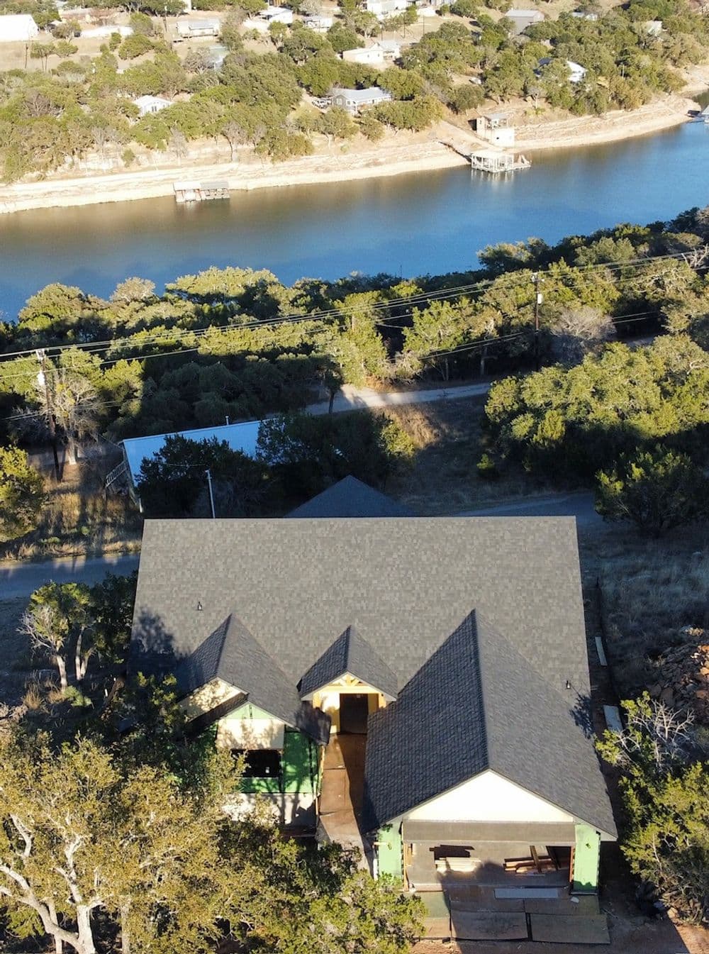 Aerial view of a modern house near a river, surrounded by trees and natural landscape.