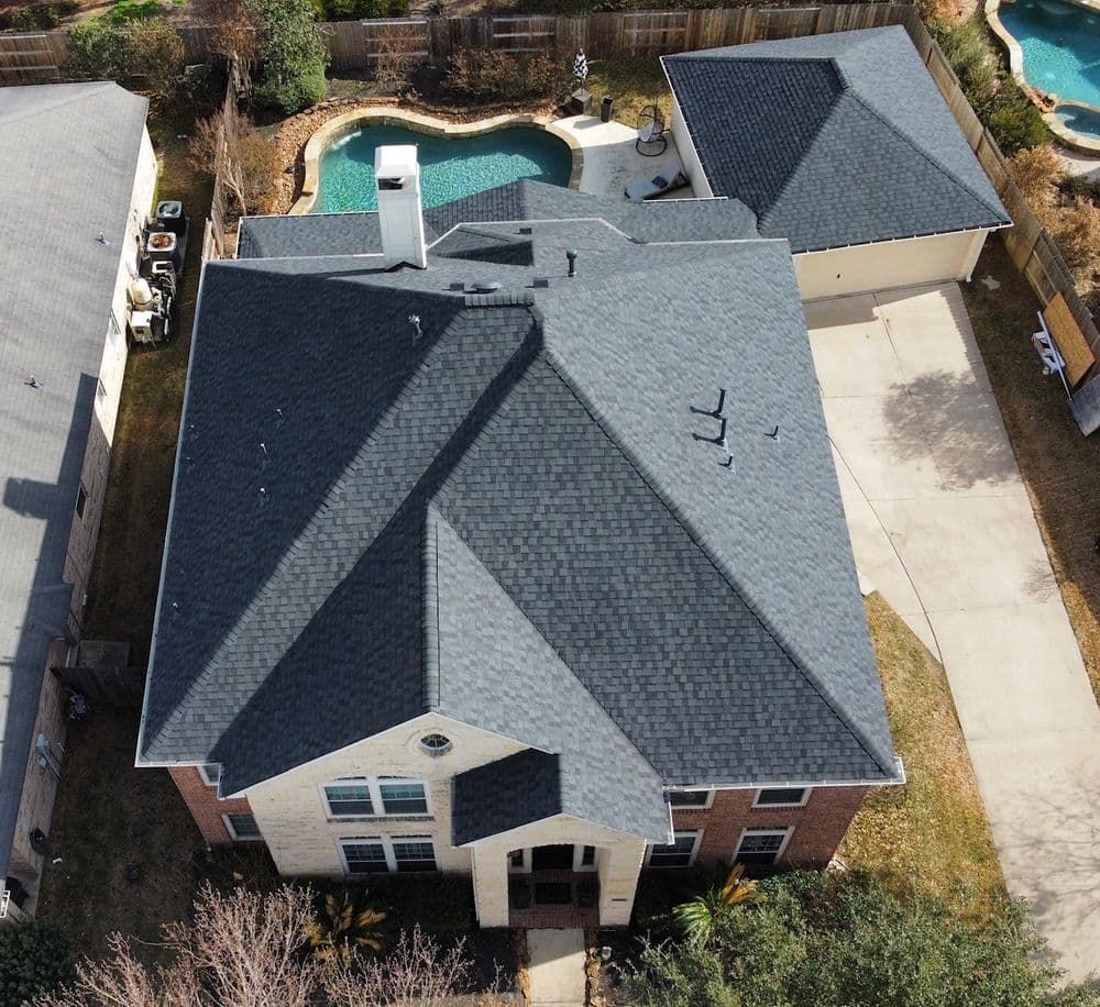 Aerial view of a large home with a dark shingle roof and surrounding outdoor space.