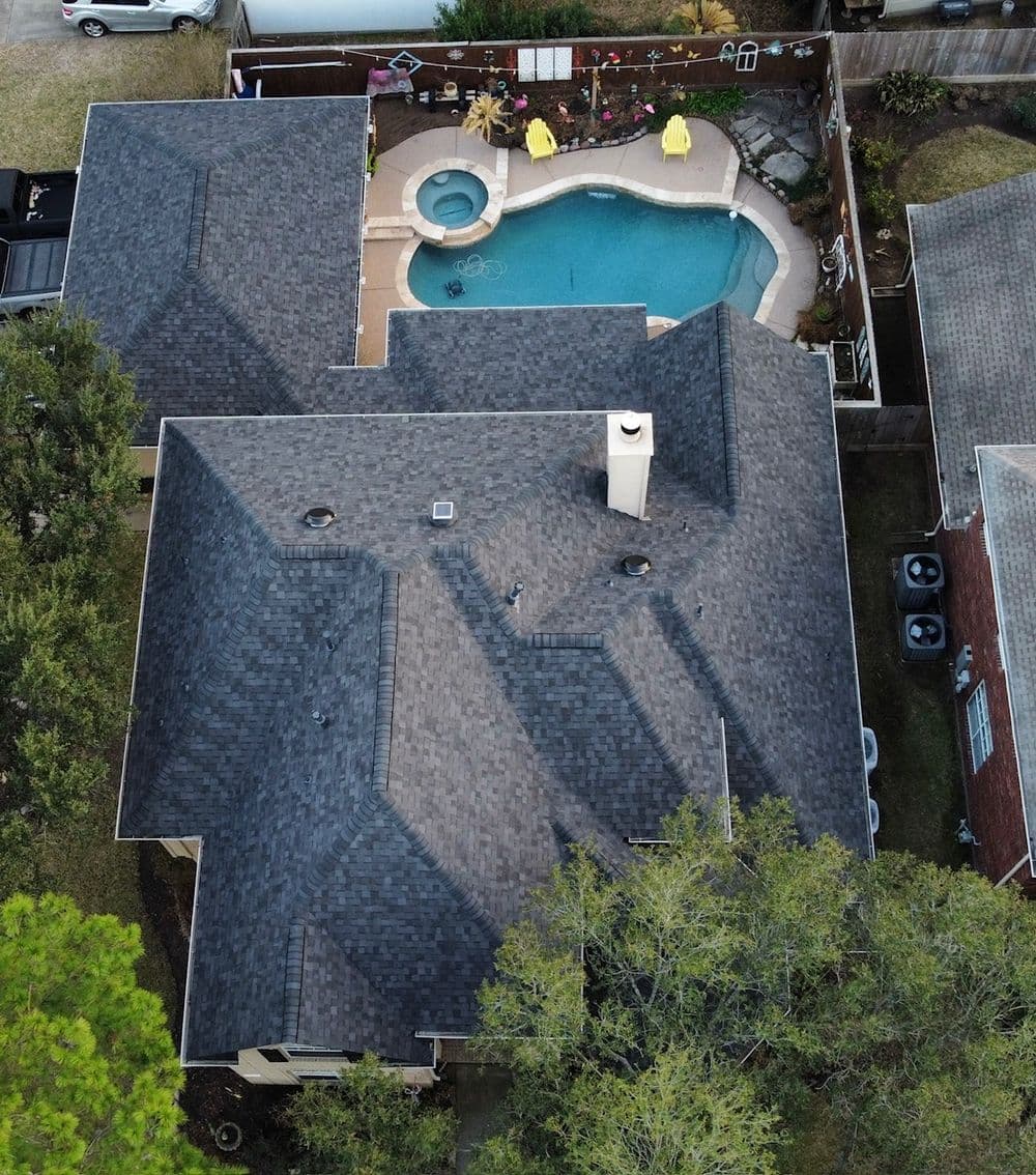 Aerial view of a house with a gray shingle roof and a backyard pool surrounded by landscaping.
