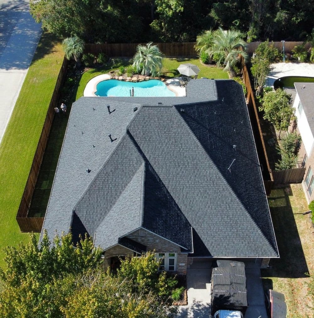 Aerial view of a modern home with a dark roof, pool, and landscaped yard.