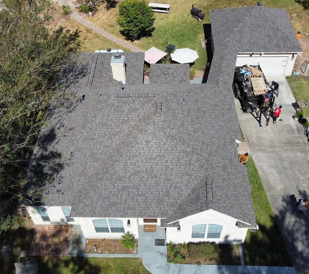 Aerial view of a residential home with gray shingles and landscaped yard.