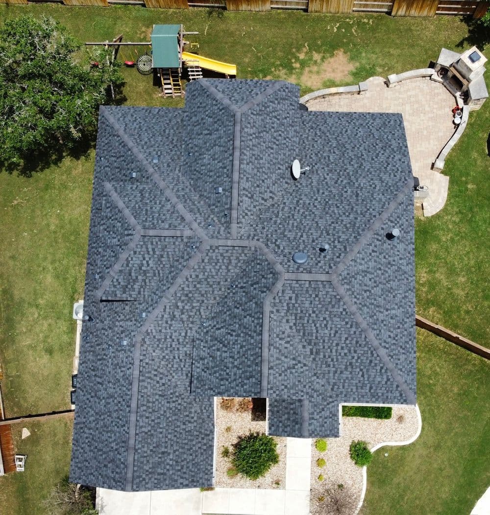 Aerial view of a dark shingle roof on a suburban home with backyard features.