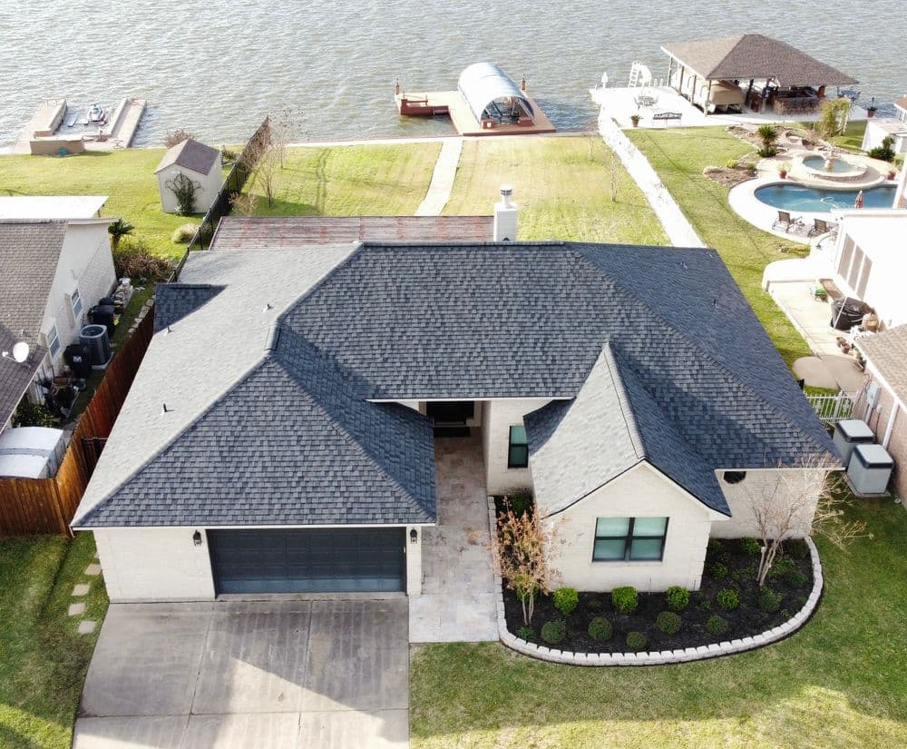 Aerial view of a modern lakeside home with landscaped yard and outdoor amenities.