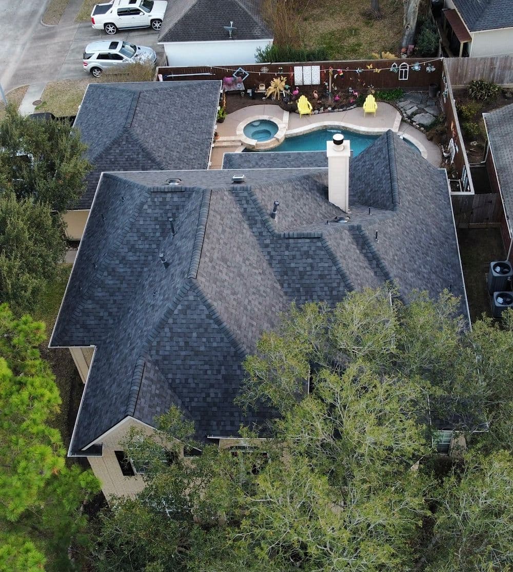 Aerial view of a house with a black roof, pool, and landscaped backyard.