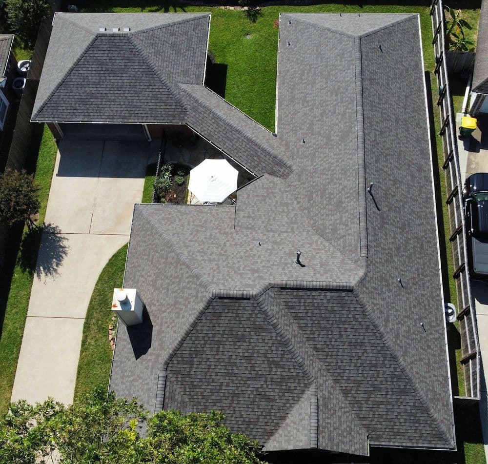 Aerial view of a modern house with a gray shingle roof and adjacent driveway.