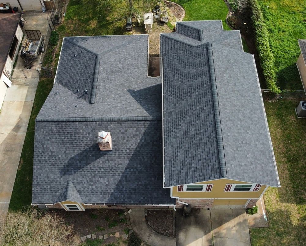 Aerial view of a two-story house with gray shingles and landscaped yard.