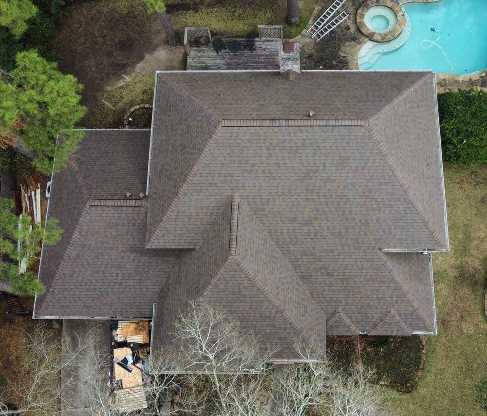 Aerial view of a large residential home with a brown shingle roof and swimming pool.