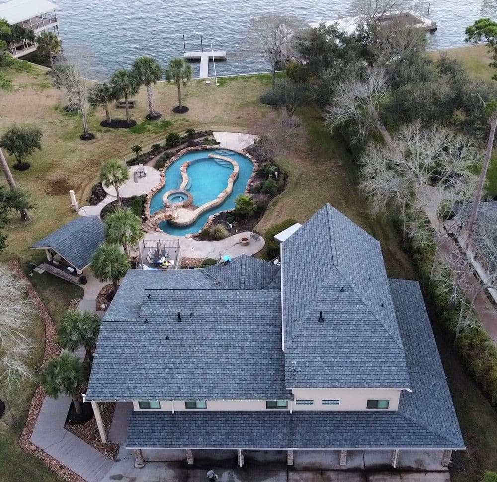 Aerial view of a waterfront home with a pool and landscaped yard, palm trees surrounding the area.