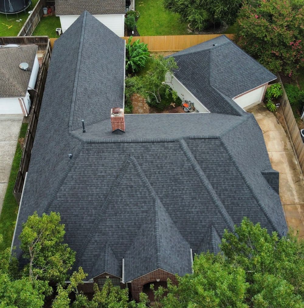 Aerial view of a modern home with a dark shingle roof and surrounding greenery.