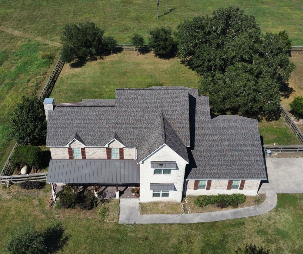 Aerial view of a modern two-story house with a large yard and surrounding greenery.
