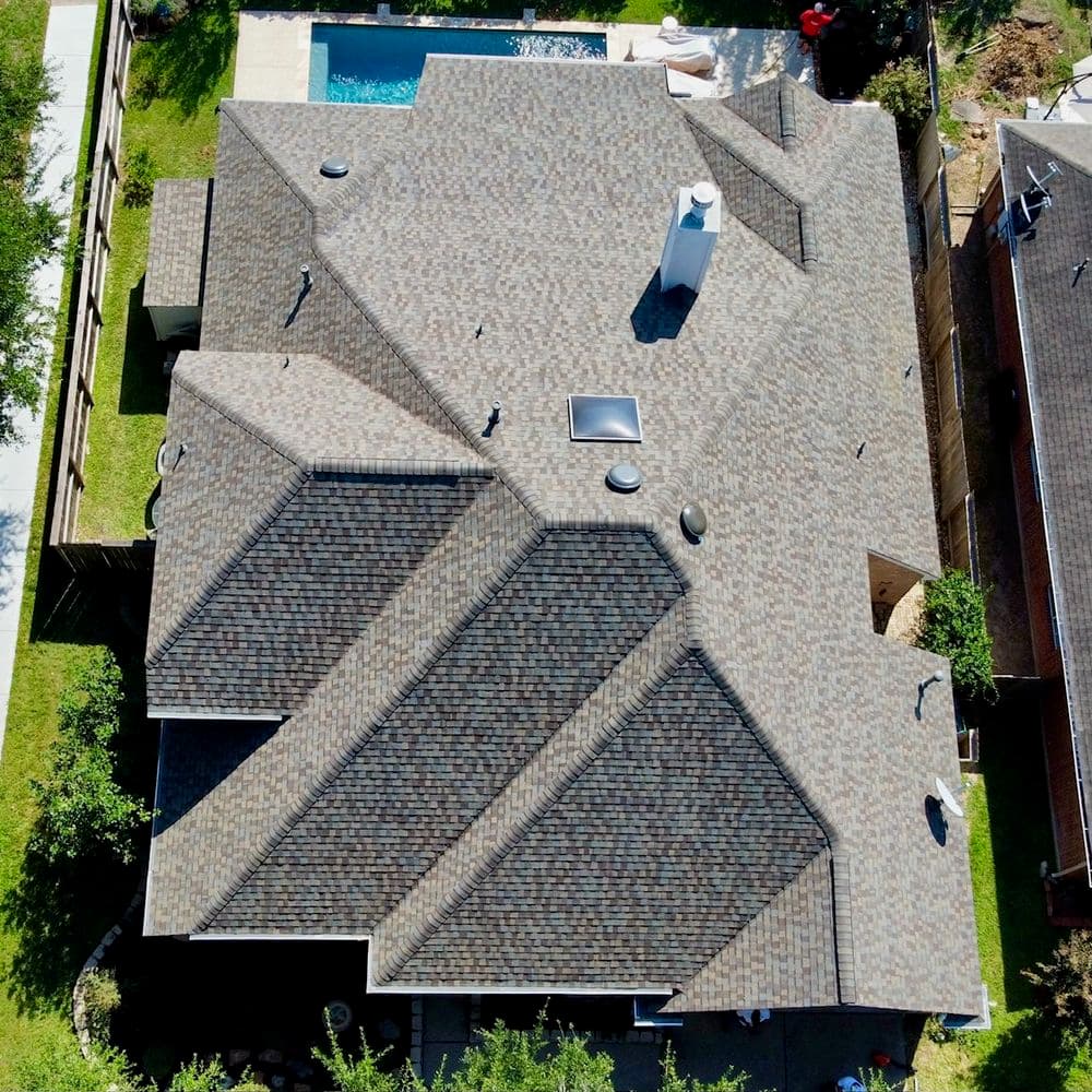 Aerial view of a multi-pitched roof with shingles and a pool in the backyard.