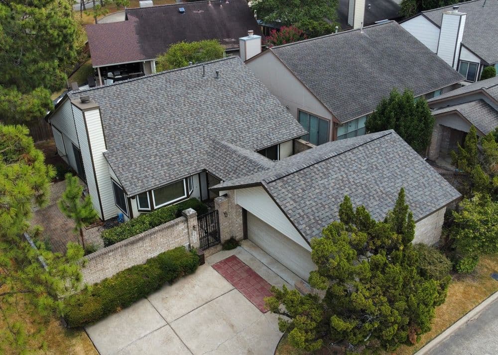 Aerial view of a residential home with a gray shingle roof and landscaped yard.