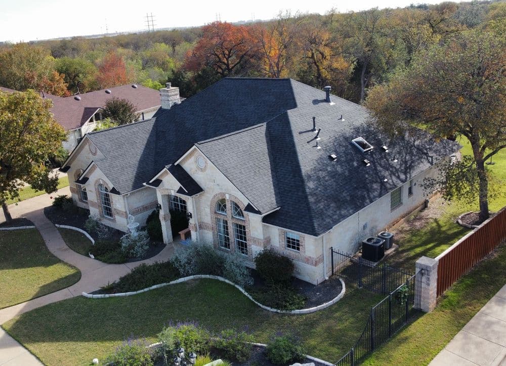 Aerial view of a modern house with a black roof and landscaped yard in a suburban area.