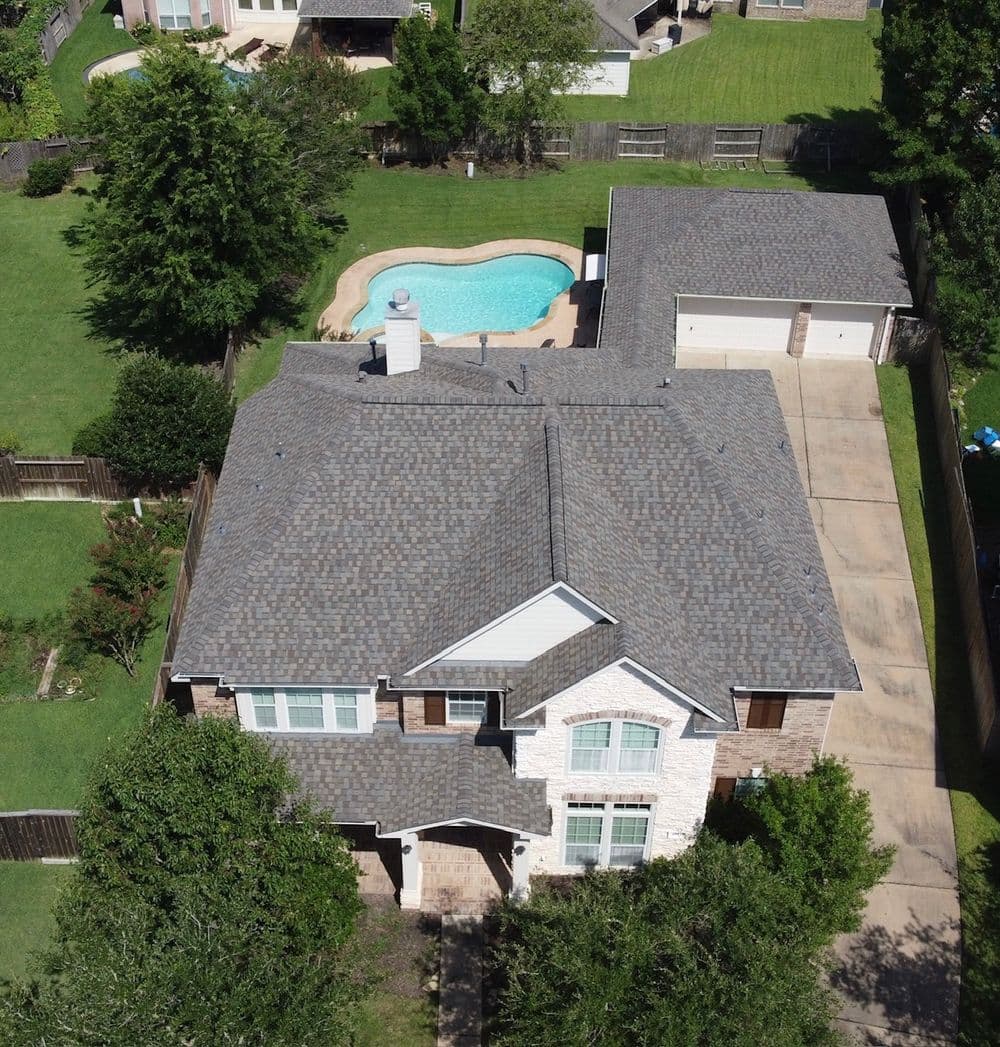 Aerial view of a beautiful suburban home with a pool and garage surrounded by greenery.