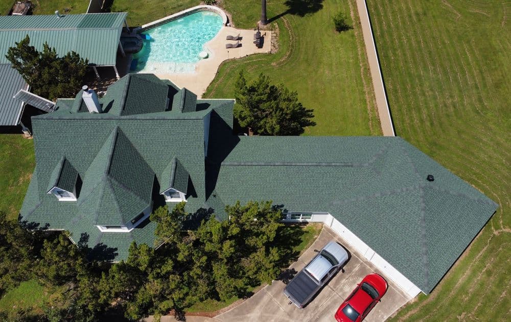 Aerial view of a green-roofed house with a pool and red cars in the driveway.