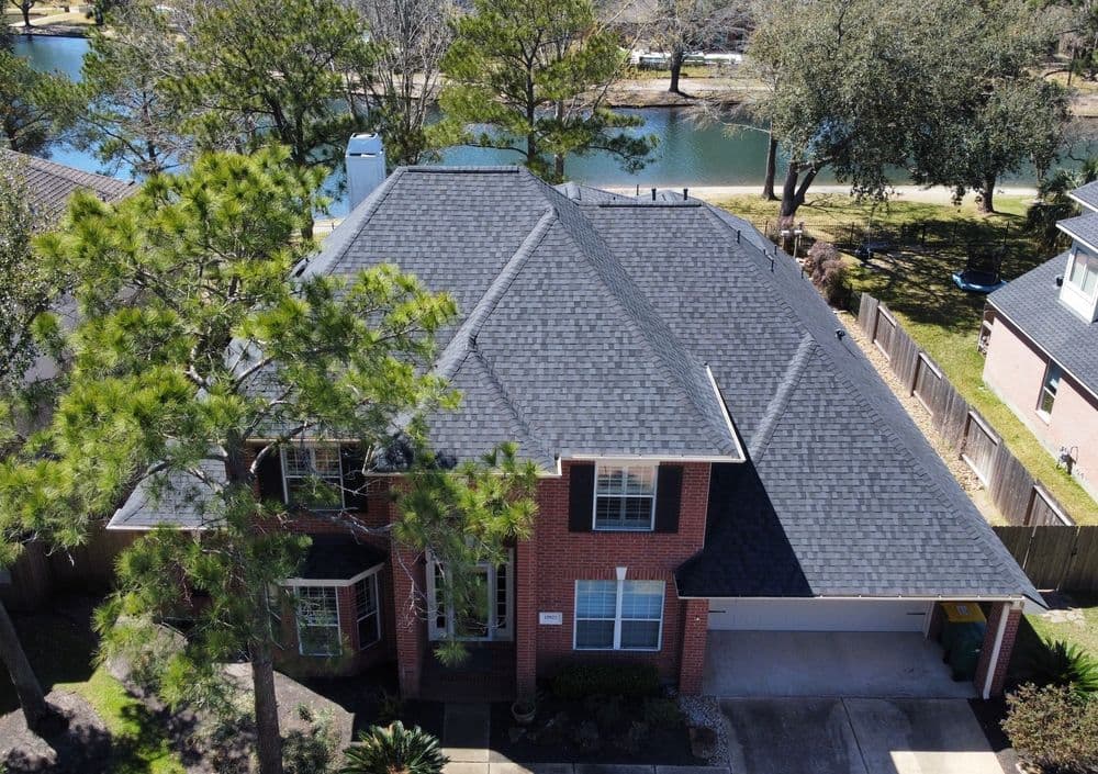 Aerial view of a residential home with a dark shingle roof near a serene waterway.