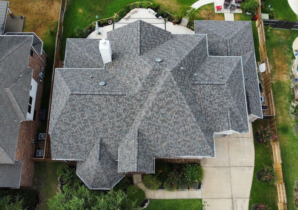 Aerial view of a modern home with a complex roof design and lush landscaping.