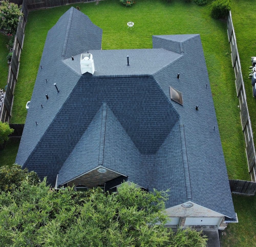 Aerial view of a residential roof with dark shingles, featuring a skylight and chimney.