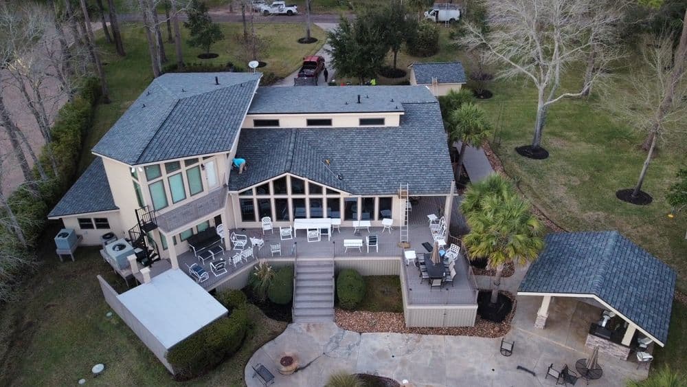 Aerial view of a modern home with a large deck, surrounded by trees and outdoor seating.