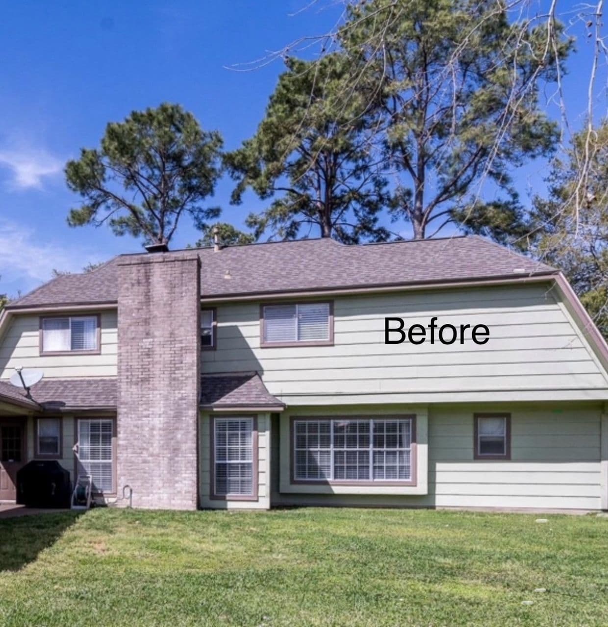 Two-story house with gray siding and green accents, shown before renovation, surrounded by trees.